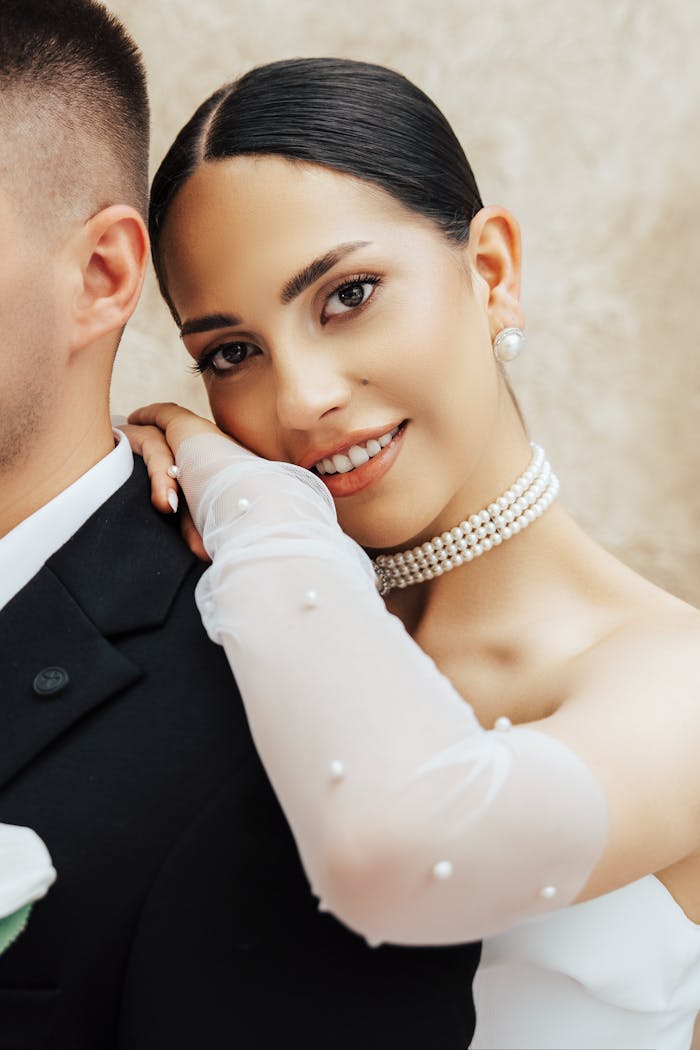Home Close-up of a smiling bride with pearl jewelry, leaning on her groom in Antalya.